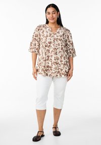 Blusa beige con stampa animalier marrone, scollo a V e maniche a palloncino, abbinata a pantaloni capri bianchi e sandali neri con cinturini.