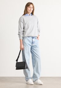 Felpa grigia chiara, camicia con colletto blu sotto, jeans azzurri, sneaker bianche e una borsa a tracolla nera con chiusura a patta.