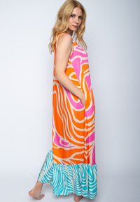 Maxi sukienka w żywych kolorach z abstrakcyjnym wzorem zebry w odcieniach pomarańczowym, różowym i kremowym, z turkusowym falbaniastym dołem i bocznymi kieszeniami.