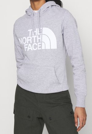Osoba nosząca jasnoszary kaptur z białym logo "THE NORTH FACE", dobrany do ciemnozielonych spodni bojowych.