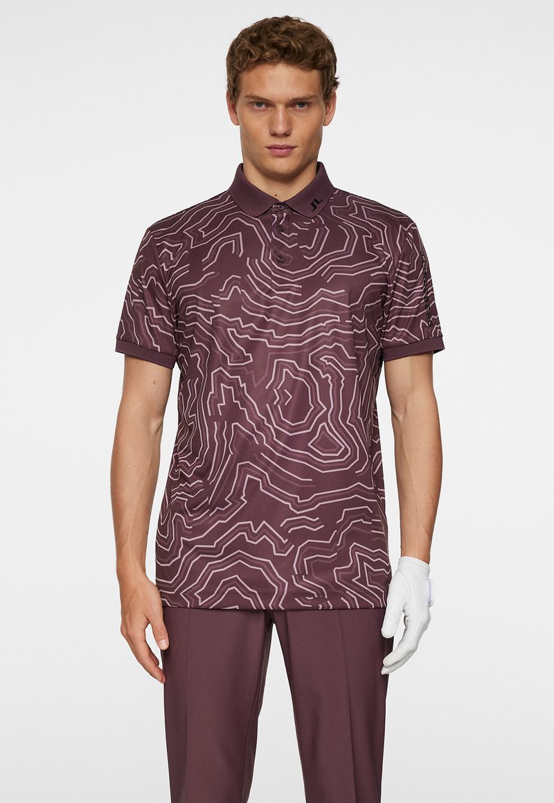 Pikétröja i djup lila med ett topografiskt linjemönster i ljuslila, korta ärmar och en krage med tre knappar.