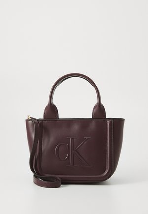 Borsa a mano in pelle color bordeaux con due manici, tracolla removibile e logo "cK" impresso sulla pannello frontale.