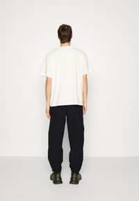 Witte katoenen T-shirt met korte mouwen, losse pasvorm, gecombineerd met donker navy broek. Draag het met zwarte chunky sneakers. Eenvoudig ontwerp.