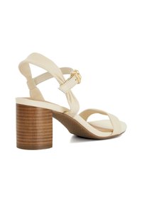 Sandale à talon haut beige avec un talon en bois, présentant des brides croisées, une semelle intérieure rembourrée et un accent de boucle dorée sur la bride de cheville.