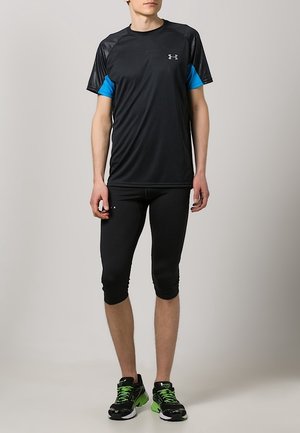 Sort atletisk t-shirt med blå aksentærmer, parret med sorte leggings til knæene og sorte sneakers med grønne detaljer.