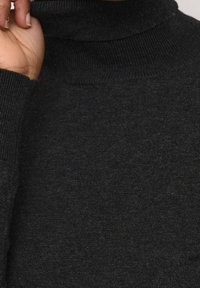 Czarny sweter z golfem o prążkowanym kołnierzu i mankietach, wykonany z miękkiej, teksturowanej tkaniny. Materiał ma subtelną połyskliwość i elastyczność.