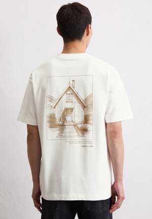 White cotton t-shirt featuring a brown sketch of a house on the back. Short sleeves, relaxed fit, and a round neckline.