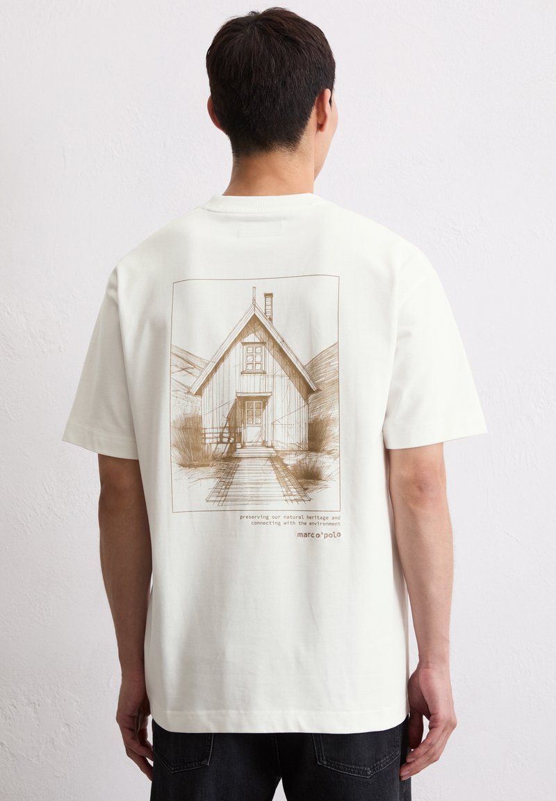 Biała koszulka z bawełny z brązowym szkicem domu na plecach. Krótkie rękawy, luźny krój i okrągły dekolt.