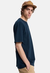 Μπλούζα από βαμβάκι σε ναυτικό μπλε χρώμα με κοντά μανίκια, στρογγυλή λαιμόκοψη, άνετη εφαρμογή και υφασμένη ετικέτα στο πλάι. Συνδυάζεται με  καφέ καπέλο.