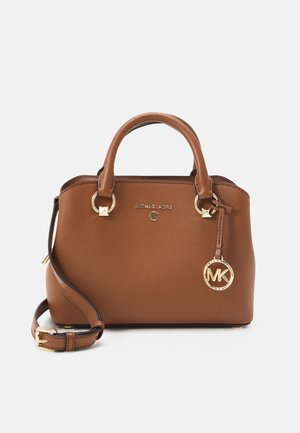 Brązowa skórzana torebka Michael Kors z podwójnymi uchwytami, regulowanym paskiem na ramię oraz złotym breloczkiem z logo MK zawieszonym na jednym uchwycie.