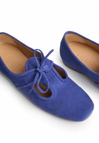 Niebieskie zamszowe balerinki z otwartymi wycięciami i detalem w postaci kokardki z przodu. Gładkie wnętrze z brązową wkładką i zaokrąglonym, miękkim kształtem palców.