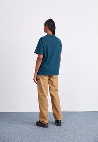 Dark teal short-sleeved shirt with a relaxed fit, paired with tan cargo pants. Black platform shoes complete the outfit.