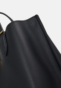 Zwarte leren handtas met een gestructureerde afwerking, een gebogen bovenzijde en een smalle handgreep. Goudkleurige metalen accenten zijn zichtbaar.