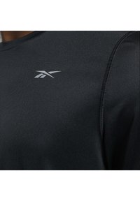 Svart träningsskjorta i texturerad tyg. Har rund halsringning och en liten silverlogotyp på vänster bröst område.