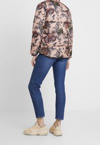 Chaqueta acolchada con una base rosa y patrones multicolores de flores y animales, combinada con jeans azules y zapatillas de colores claros.