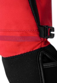 Materiale softshell rosso con accenti e cuciture nere. Presenta una fibbia nera e un'etichetta goffrata "SOFTSHELL". Texture liscia.