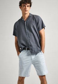 Camicia a maniche corte grigio antracite con colletto; abbinata a pantaloncini azzurri chiari e una cintura nera; vestibilità casual e rilassata.