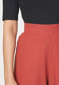 Svart ribbad t-shirt med korta ärmar, ihopparad med högmidjade ribbade byxor i rostfärg med bred midja och vertikal textur.