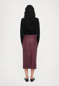 Jupe midi en cuir bordeaux avec une texture lisse et des détails de couture, associée à un haut noir à manches longues et des chaussures plates noires.