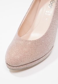 Escarpin à talon haut rose clair en tissu texturé avec un léger effet scintillant, bout rond et doublure intérieure lisse. Détail de plateforme basse.