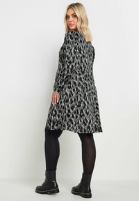 Sukienka w czarno-szare cętki z długimi rękawami, rozkloszowanym dołem i okrągłym dekoltem, w połączeniu z czarnymi botkami za kostkę i legginsami.
