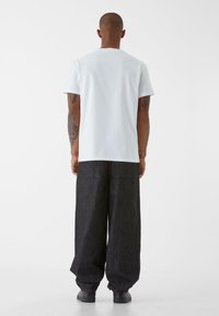 T-shirt bianco a maniche corte abbinato a pantaloni in denim scuro a vestibilità larga. Design semplice, texture morbida, senza motivi o grafiche visibili.