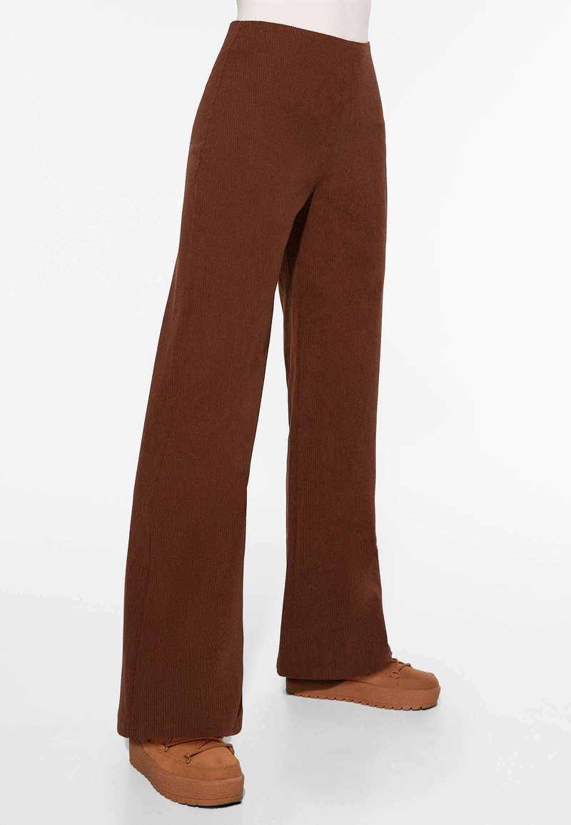 Bruine geribbelde wijde broek met hoge taille, voorzien van een textuurafwerking en zijzakken, gecombineerd met lichtbruine plateauschoenen.