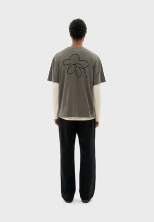 T-shirt en coton gris avec un dessin de fleur noire au dos, superposé sur une chemise à manches longues crème, assorti avec un pantalon noir.