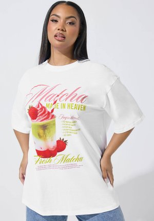 Junge Frau trägt ein weißes, übergroßes T-Shirt mit einem bunten Matcha- und Erdbeer-Dessert-Motiv und Rezepttext.