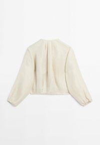 Crème-kleurige blouse met lange mouwen, voorzien van gathered elastische manchetten en plooien onder de halslijn op de achterkant, plat gelegd op een witte ondergrond.
