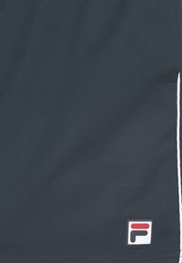 Mörk marinblå tyg med vit vertikal rand till höger och ett litet FILA-logomärke i det nedre högra hörnet.