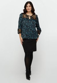 Blusa nera con stampa leopardata turchese, scollatura e maniche in pizzo, abbinata a una gonna a tubino nera e tacchi alti neri.