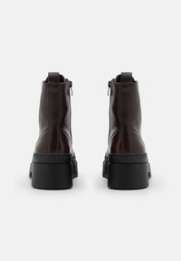 Cizme de piele maro închis, netede, până la gleznă, cu o talpă platformă groasă neagră și fermoare laterale. Au un design minimalist cu o cusătură.