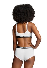 Sostén deportivo blanco y bragas de talle alto a juego con banda del logo de Puma en negro. Tejido suave, tirantes ajustables y diseño minimalista.