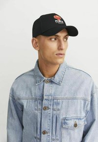 Gorra de béisbol negra con diseño floral y texto "PLACE", combinada con una chaqueta de mezclilla azul claro con grandes botones y cuello.