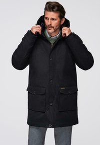 Černá parka s kapucí, která má zapínání na knoflíky, dvě velké přední kapsy a strukturovanou tkaninu. Interiér je podšit kontrastním vzorem.