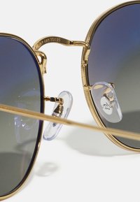 Occhiali da sole in metallo dorato con lenti nere sfumate, dotati di naselli trasparenti e un design del ponte dettagliato. Tempie sottili e dritte.