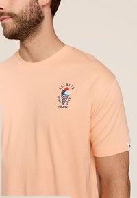 Perzikkleurig katoen t-shirt met een geborduurd ijsje logo en de tekst "GELATTO LOVERS CLUB" in marineblauw op de borst.