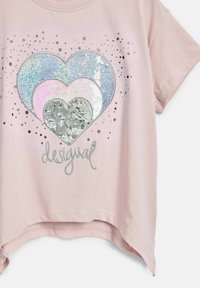 T-shirt rosa chiaro a maniche corte con un design di cuore in paillettes multicolore e la parola "desigual" in argento. Tessuto morbido con una vestibilità comoda.