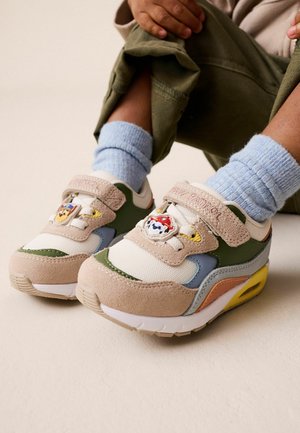 Child wearing colorful sneakers with Paw Patrol character badges, light blue socks, and rolled-up green pants.