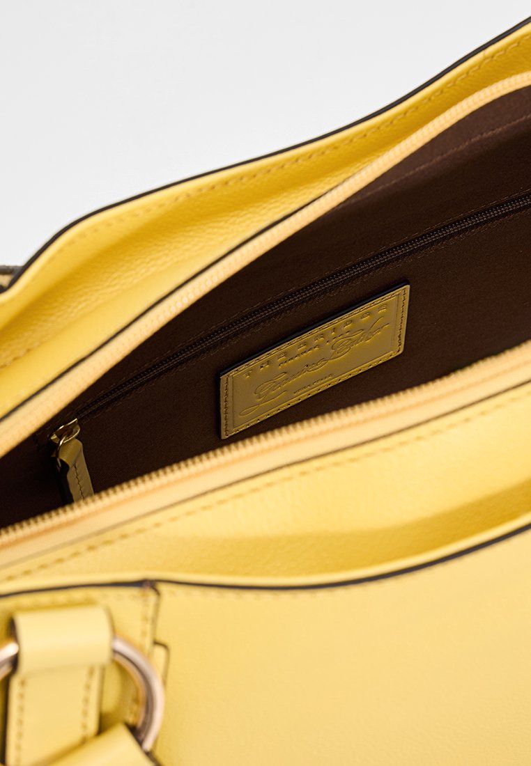 Interno di una borsa a mano gialla in pelle con una fodera marrone, dotata di una tasca con zip e un'etichetta logo dorata. Texture liscia e design strutturato.