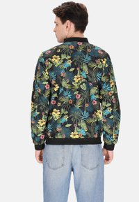 Jachetă bomber florală cu o bază neagră și flori și frunze multicolore vibrante. Guler și mansete ribbate, material ușor.