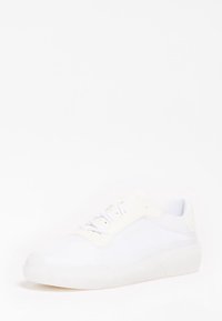 Chaussure de sport blanche avec une tige synthétique lisse, des panneaux en mesh texturé, un laçage traditionnel et une semelle en caoutchouc semi-transparente.