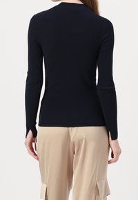 Marinblå randig långärmad topp med sidslitsar vid fållen. Har en figurnära silhuett och rund halsringning, i kombination med beige satinbyxor.