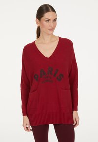 Roter Strickpullover mit V-Ausschnitt, zwei Vorderaschen und schwarzem Text "PARIS mon amour". Rippdetails am Saum und an den Bündchen.