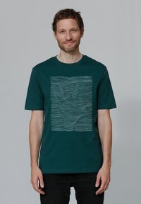 Donkergroene katoenen t-shirt met een handgrafiek gemaakt van witte golvende lijnen. Korte mouwen en een ronde hals.