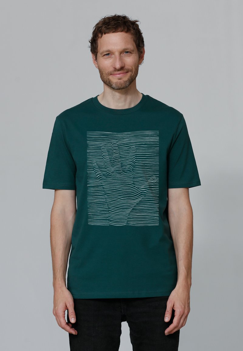 Donkergroene katoenen t-shirt met een handgrafiek gemaakt van witte golvende lijnen. Korte mouwen en een ronde hals.