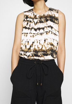 Sleeveless top with black, brown, and white abstract pattern paired with black drawstring pants, hands in pockets.