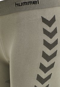 Gröna leggings gjorda av elastisk tyg med en ribbad midja och svarta chevronmönster längs sidan. Varumärkeslogotyp synlig på toppen.