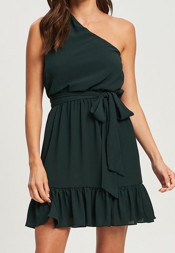 Sukienka na jedno ramię w ciemnozielonym kolorze, uszyta z lekkiego materiału, z dopasowaną talią i falbaniastym dołem. W komplecie jest pasujący pasek do wiązania.